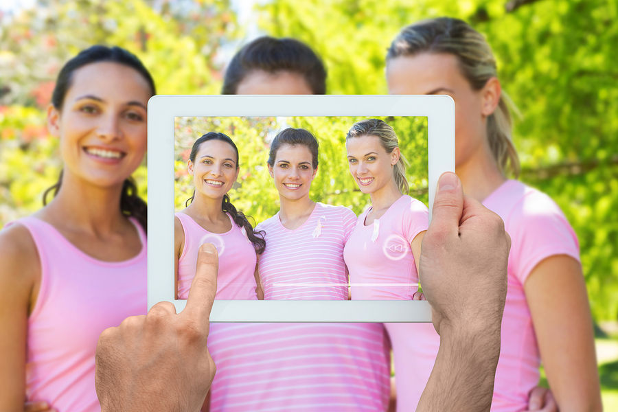 Hand holding tablet pc against smiling women in pink for breast cancer awareness